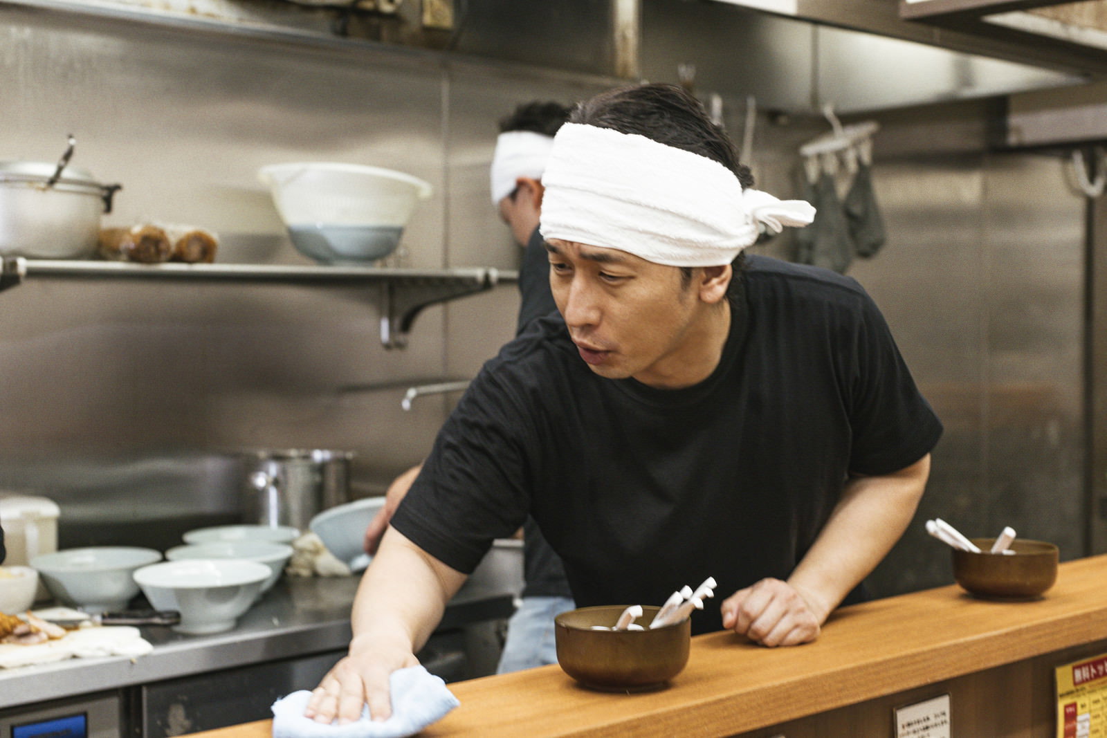 白いバンダナを巻いてラーメン店の厨房で作業する男性店員［モデル：大川竜弥］