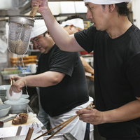 ラーメン厨房で麺の湯切りをするアルバイト店員の写真