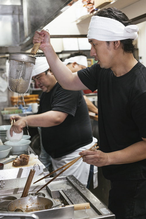 ラーメン厨房で麺の湯切りをするアルバイト店員