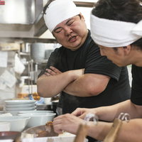 厨房でダメ出しをするラーメン店の店主と男性アルバイトの写真