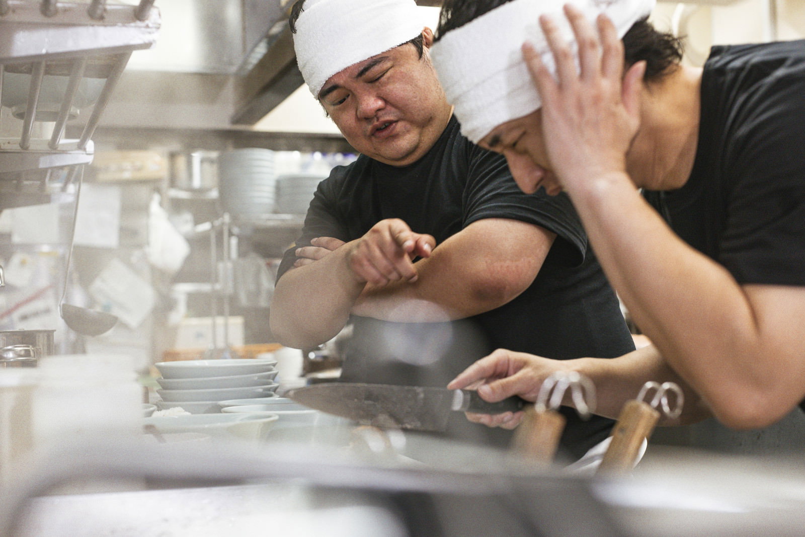 厨房でチャーシューの切り方を指導される新人と師匠［モデル：段田隼人 大川竜弥］