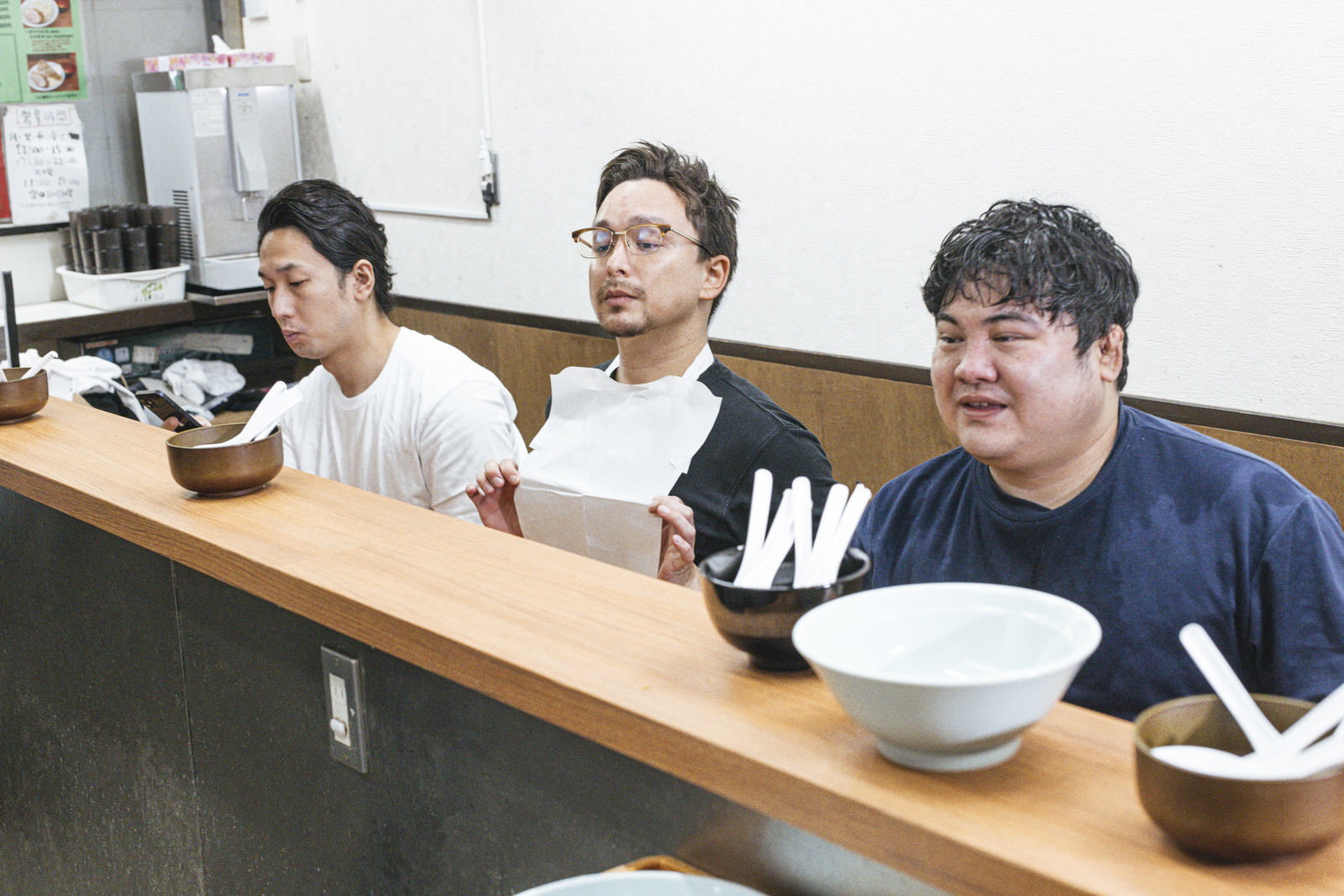 ラーメン屋の木製カウンターに座り着丼を待つ3人の男性客［モデル：大川竜弥 Max_Ezaki 段田隼人］