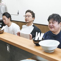 ラーメン屋のカウンターで着丼を待つ男性客たちの写真