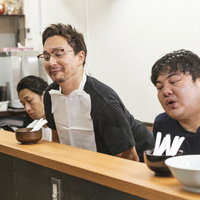 ラーメン屋のカウンターで身を乗り出す腹ペコ客の写真
