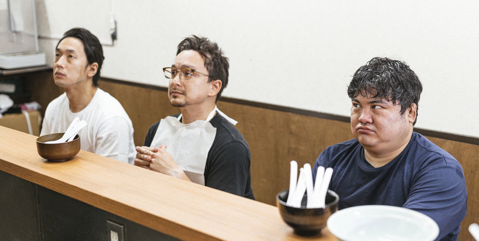 ラーメン店のカウンター席でメニューを見る3人の男性客［モデル：段田隼人 Max_Ezaki 大川竜弥］