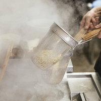 ラーメン屋の厨房でテボを使って麺の湯切りをする手元の写真