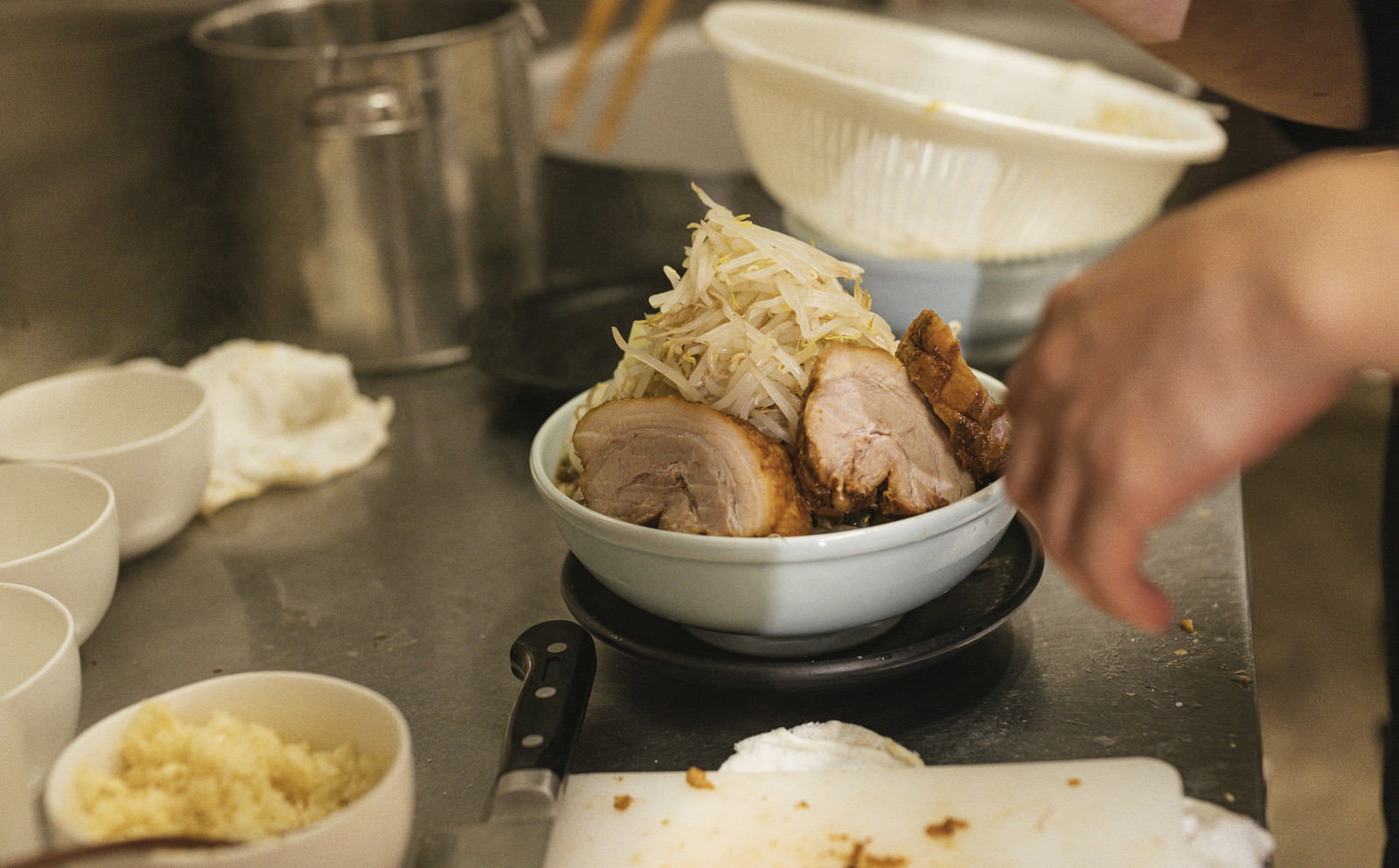 丼からはみ出るほどの大盛りチャーシューメンを厨房で盛り付けている様子