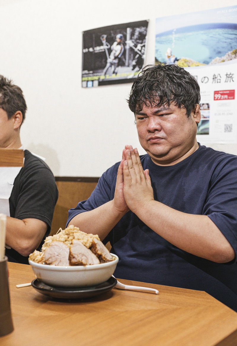 ラーメン店のカウンター席で大盛りラーメンに手を合わせる男性