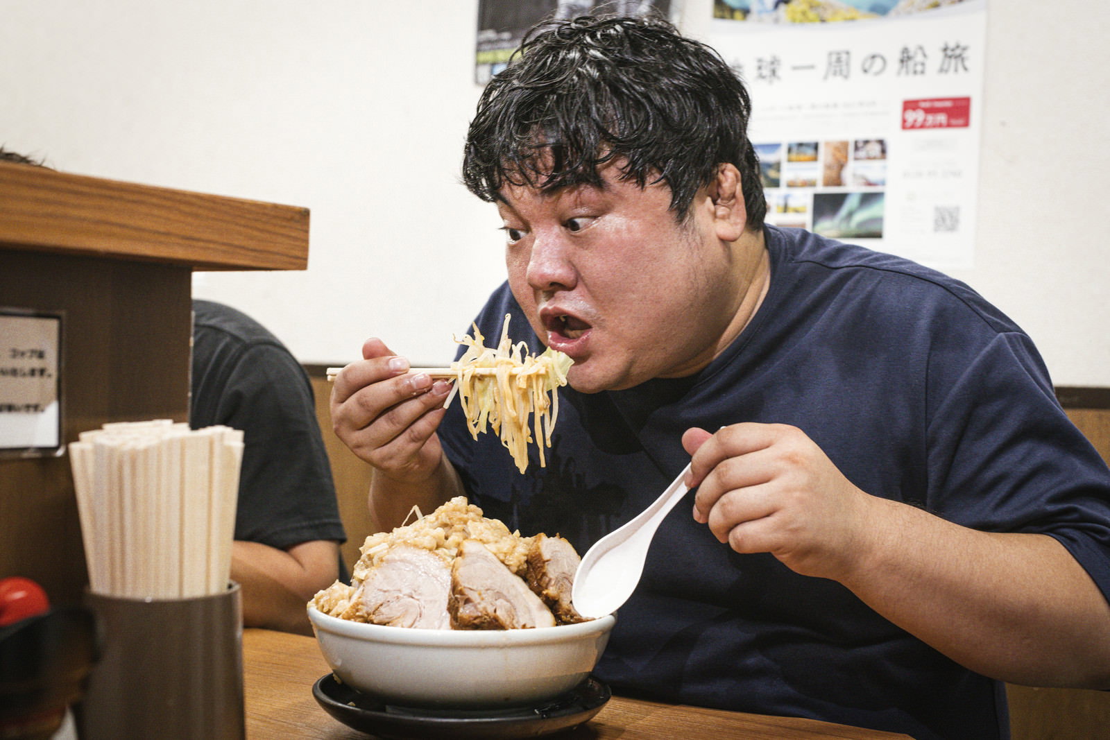 ラーメン店のカウンター席で箸を使って麺を食べる男性［モデル：段田隼人］