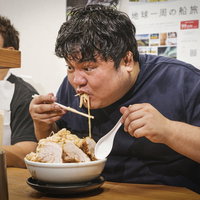 ラーメン店のカウンター席で大食い記録に挑むフードファイターの写真