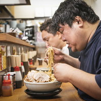 ラーメン店のカウンター席で天地返しをする常連客男性の写真