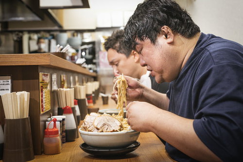 ラーメン店のカウンター席で天地返しをする常連客男性