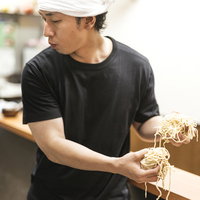 厨房で大盛りの2玉を両手で持つラーメン屋のアルバイト男性の写真