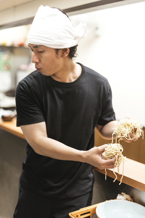 厨房で大盛りの2玉を両手で持つラーメン屋のアルバイト男性