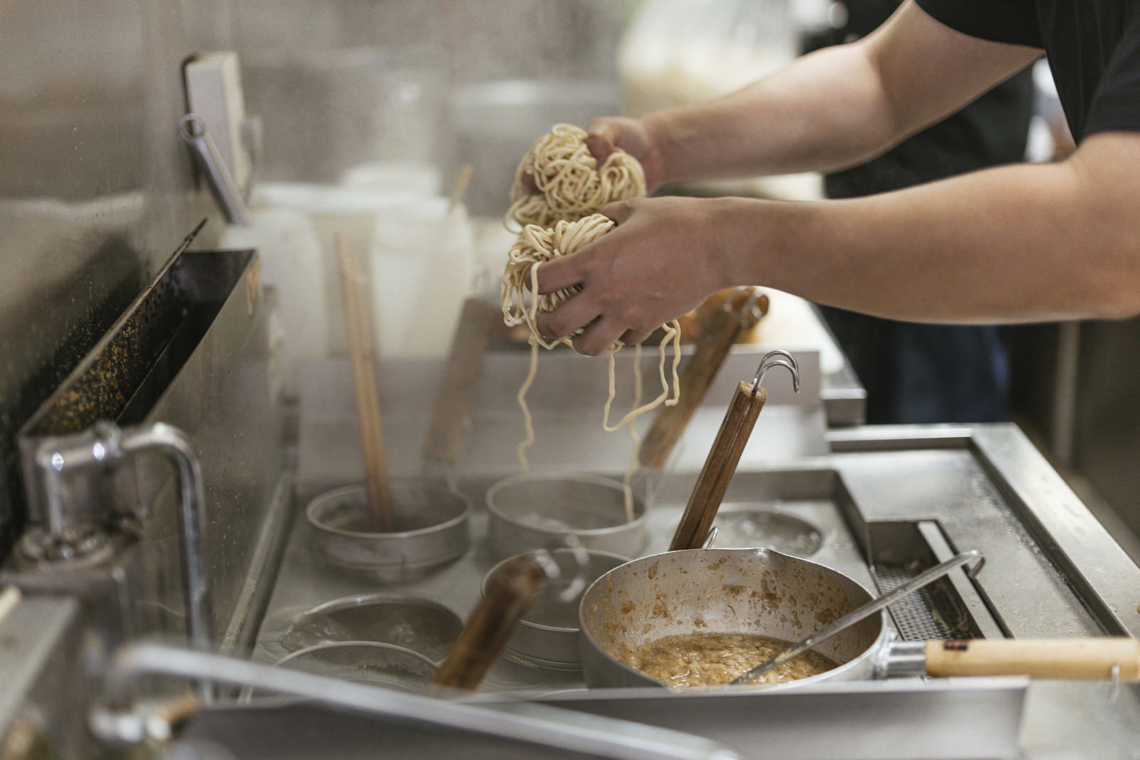 テボを使って茹でた麺の湯切りをする男性の手元