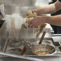 大盛りの2玉分の麺をテボで湯切りする厨房の調理風景の写真