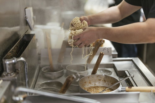 大盛りの2玉分の麺をテボで湯切りする厨房の調理風景
