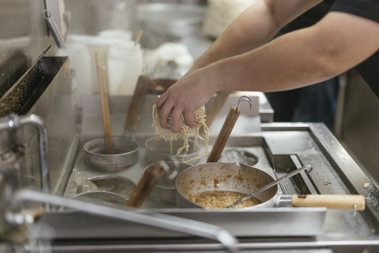 麺茹機のテボに麺を入れる男性の手元、厨房での調理風景