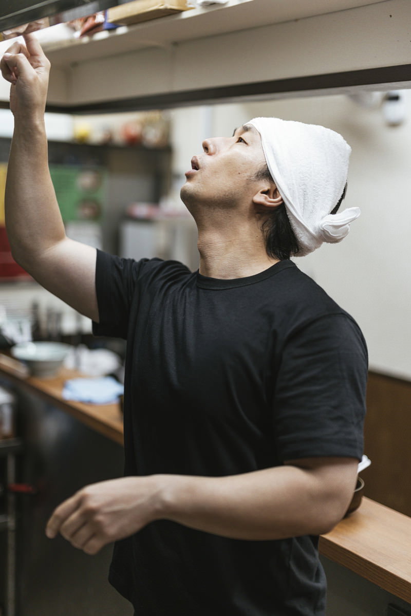 厨房でタイマーを操作するラーメン店の男性店員［モデル：大川竜弥］