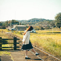 のどかな田舎町の駅のホームで立つ赤毛の女性の写真