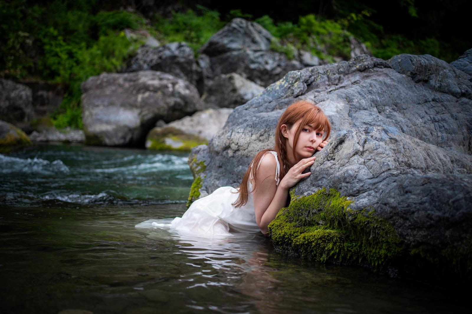 川の岩場で白いドレスを着て水に浸かり、岩に寄り掛かる女性のポートレート［モデル：ラミエル］
