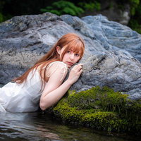 川辺の苔むした岩に寄りかかる白いドレスの女性ポートレートの写真