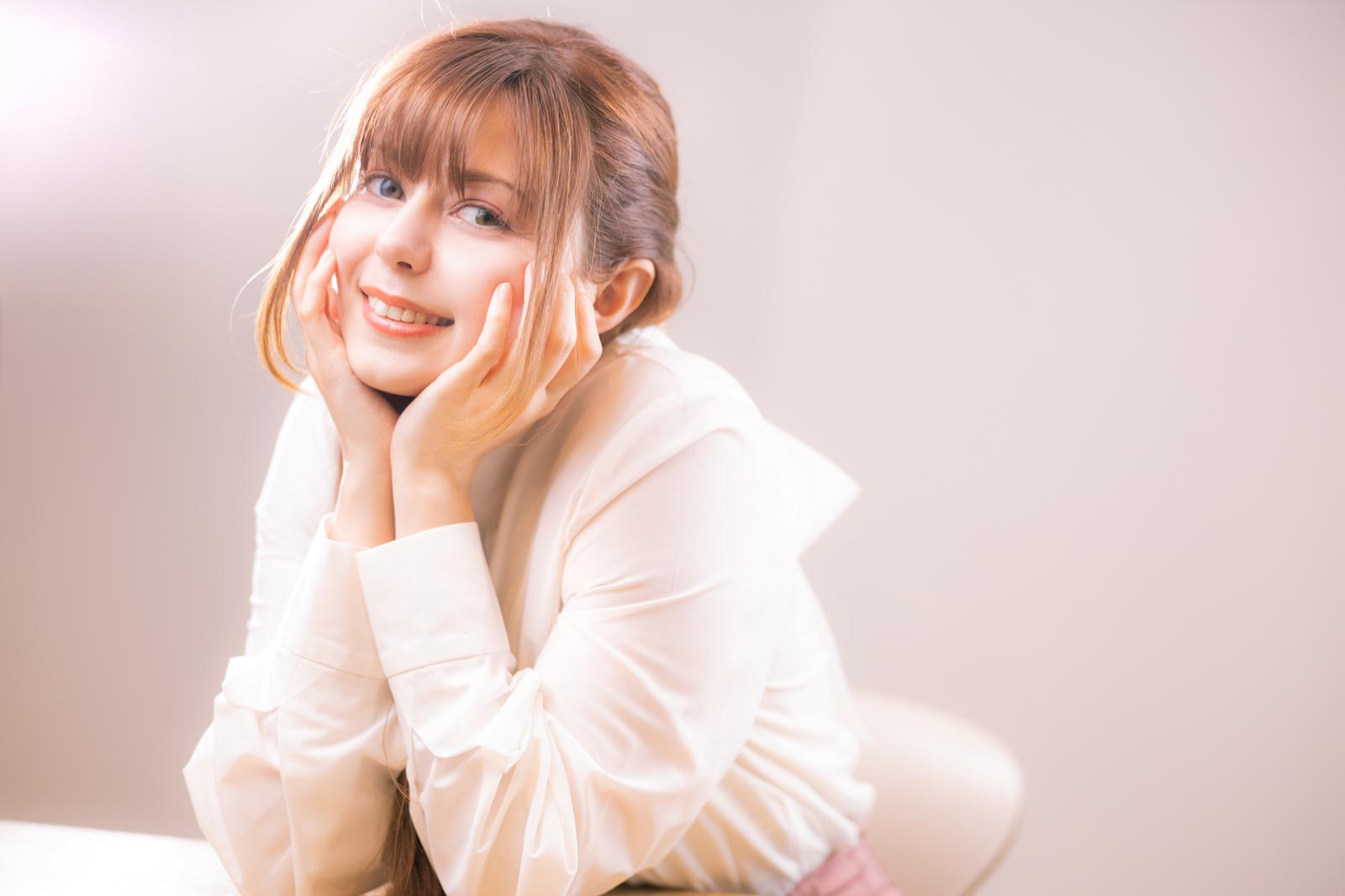 白いシャツを着た女性が頬杖をついて微笑んでいるポートレート写真［モデル：ラミエル］