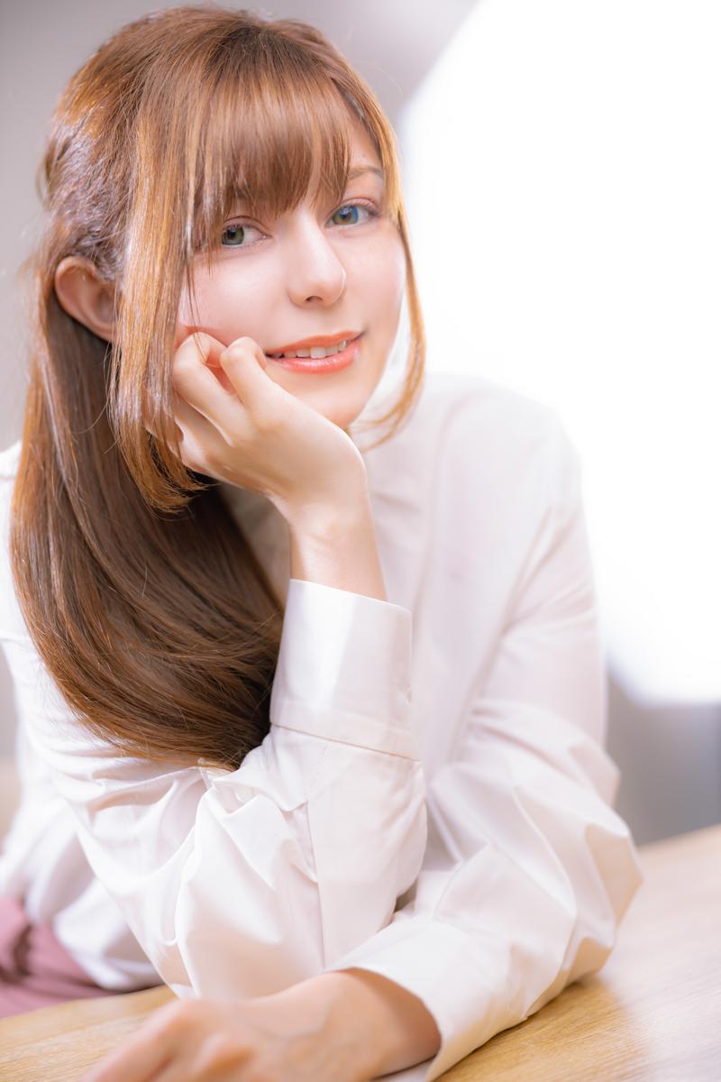 左手を頬にあてて微笑む茶髪セミロングの女性［モデル：ラミエル］