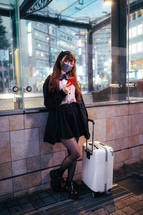 夜の駅前でキャリーケースを持って待ち合わせするハーフの地雷系女子