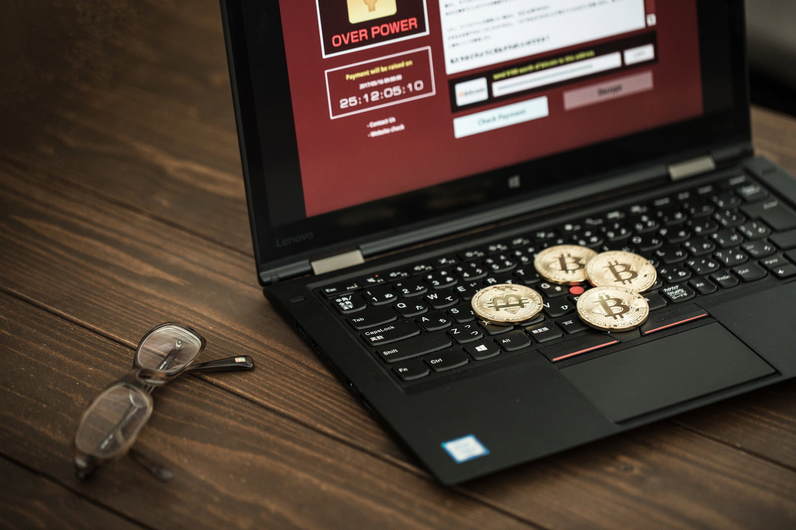 赤い警告画面が表示されたノートパソコンのキーボード上に置かれた4枚のビットコイン金貨
