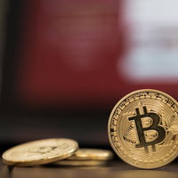 赤い画面に映るビットコインコイン、机の上の金色のコインの写真