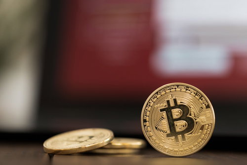 赤い画面に映るビットコインコイン、机の上の金色のコイン