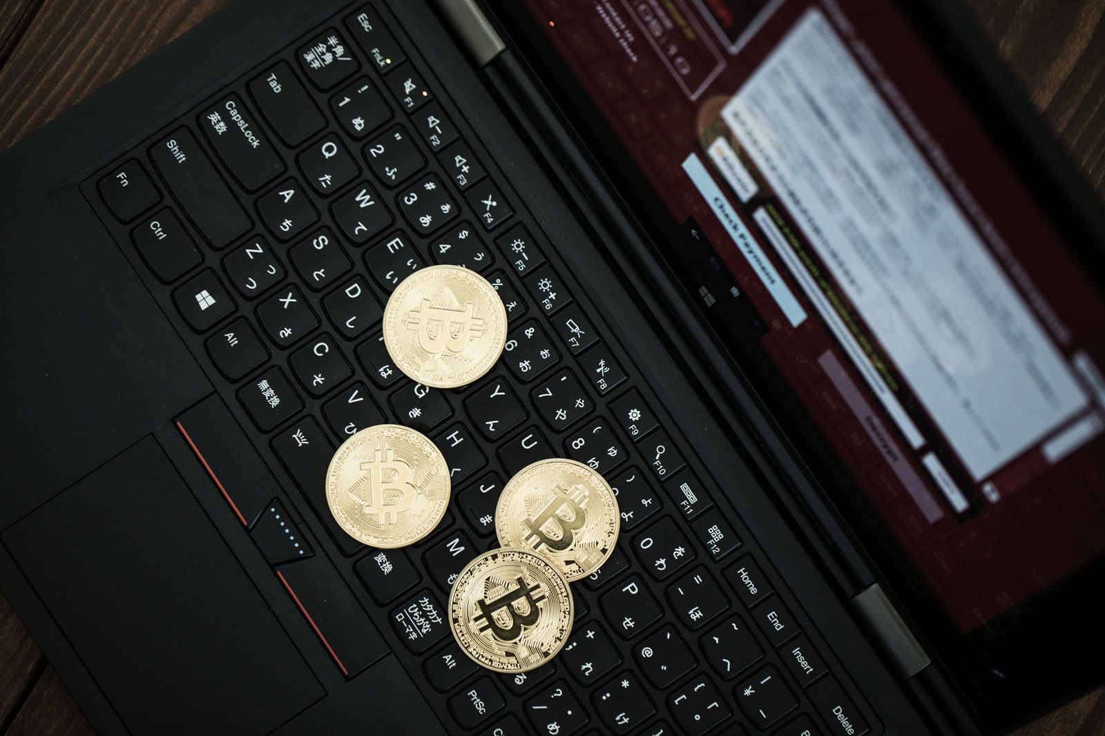 ノートパソコンのキーボードの上に置かれたビットコインコイン4枚