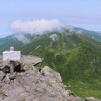 日本百名山・羅臼岳の山頂標と雲海に浮かぶ連山の写真
