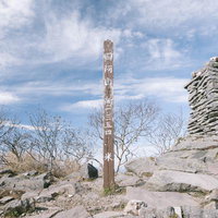 日本百名山の四阿山山頂に立つ木柱と石積みの写真