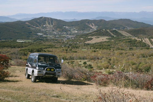 秋色に染まる菅平牧場を見下ろす黒白ツートーンのSUV作業車