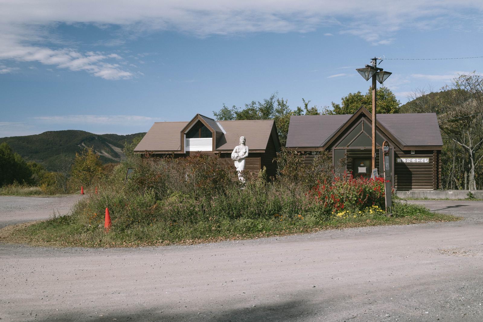 菅平ダボスバス停の白い彫像と山小屋、遠景に四阿山の山々