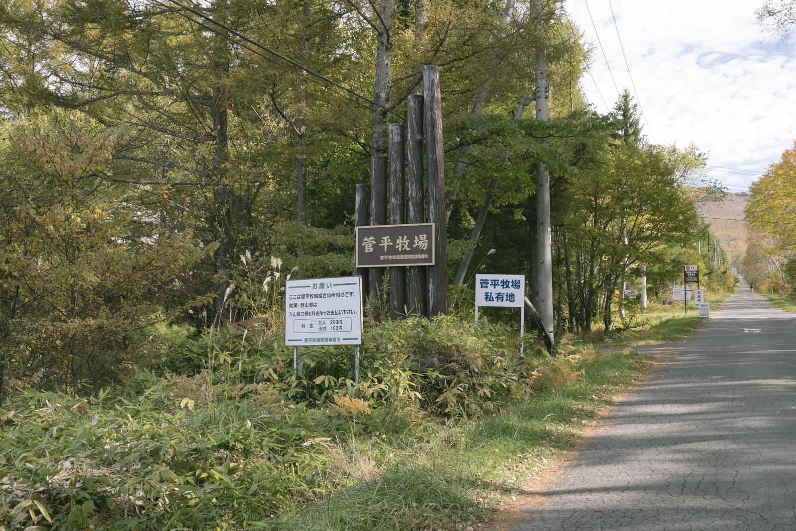 菅平牧場の看板が立つ秋の山道。奥に雑木林が広がる