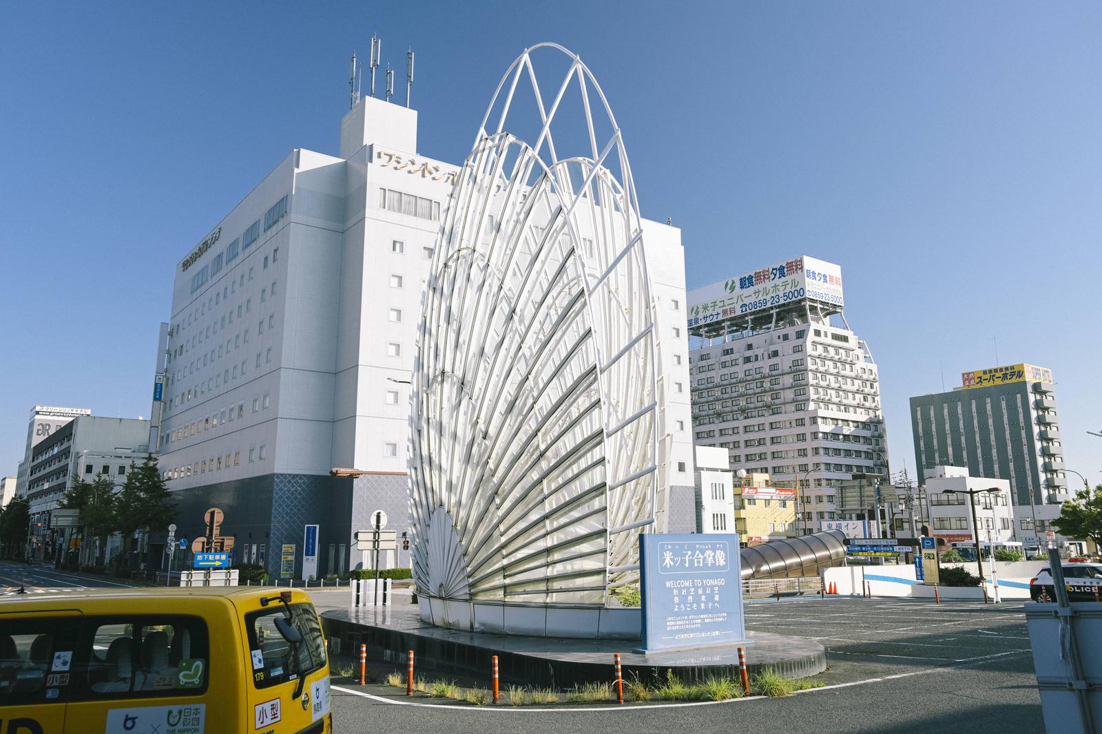 米子駅前の白い合掌像とホテルやビルが見える駅前の風景