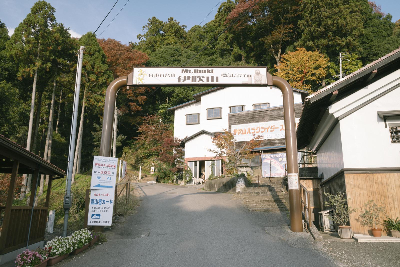 伊吹山登山口の案内ゲート。奥に白い建物と秋色の樹木が見える