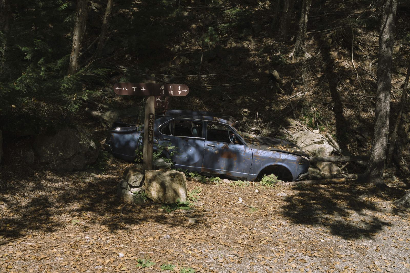 朽ちた青い廃車と金峰山の指導票が雑木林に佇む登山道