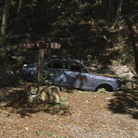 朽ちた青い車と日本百名山の道標が並ぶ山中の写真