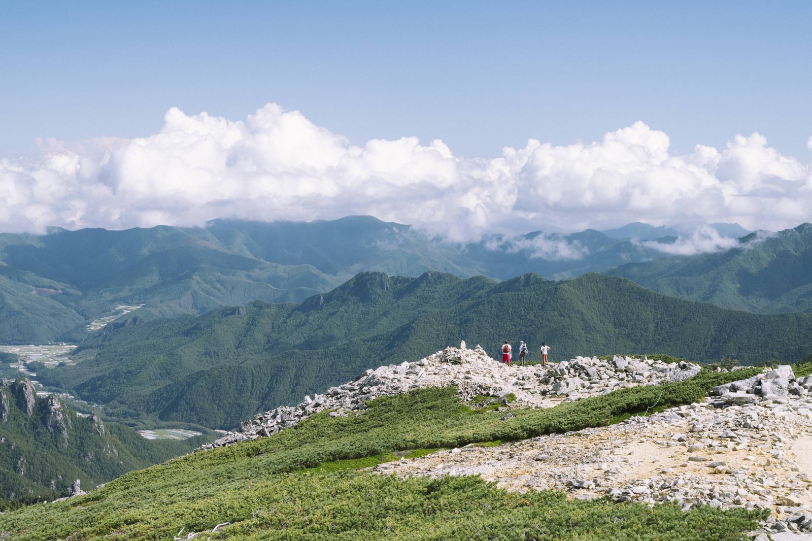 金峰山の稜線に立つ複数の登山者と遠くの山並み、白い雲が浮かぶ空