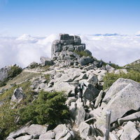 青空と雲海に映える金峰山の五丈岩と登山者の写真