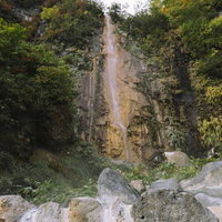 妙高山の岩壁を流れる滝、周囲の緑に囲まれた渓谷の写真