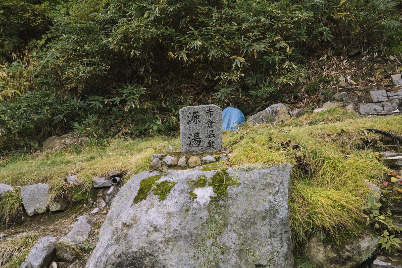 妙高山麓に立つ赤倉温泉源泉の石碑と苔むした岩、竹林
