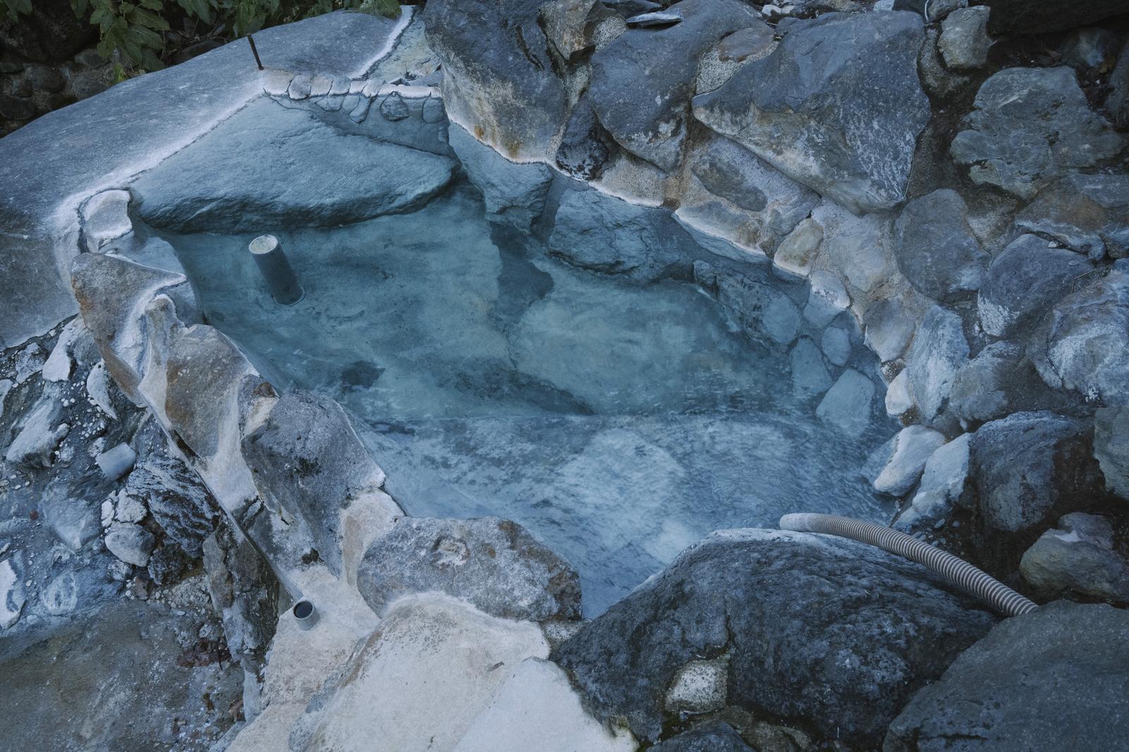 妙高山の山中にある岩風呂の野湯。澄んだお湯と調整用パイプが見える