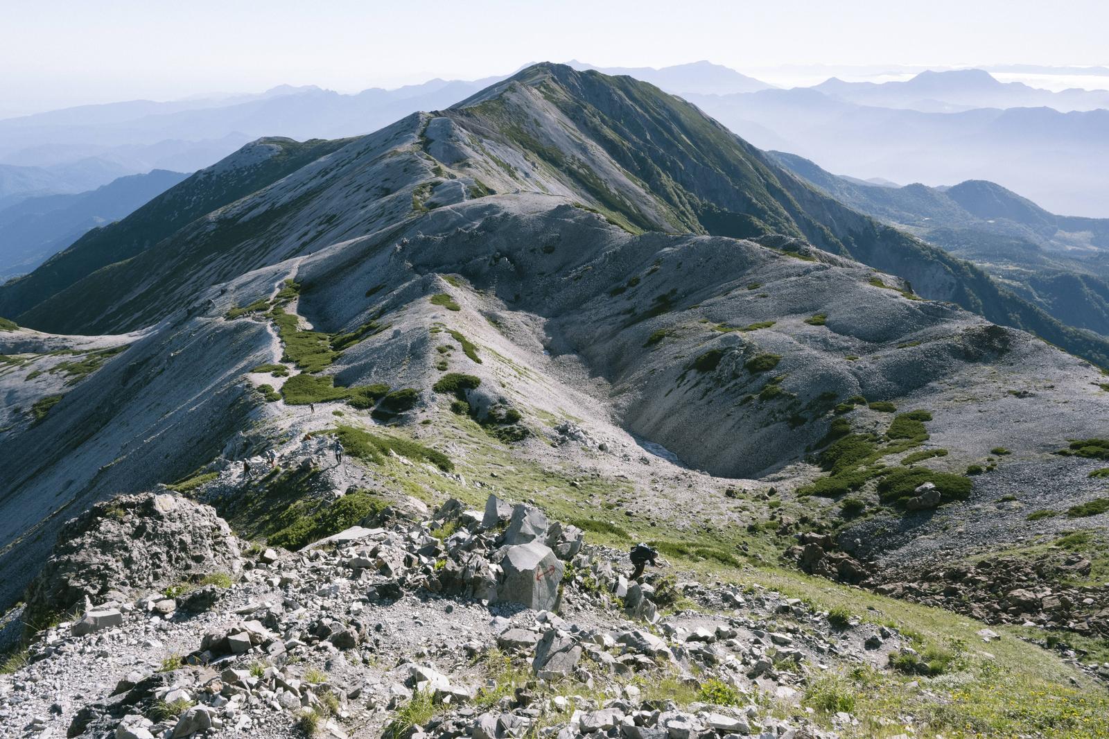 白馬岳を望む白砂の稜線。手前に岩場と低木が見え、奥に連なる山々が霞んでいる
