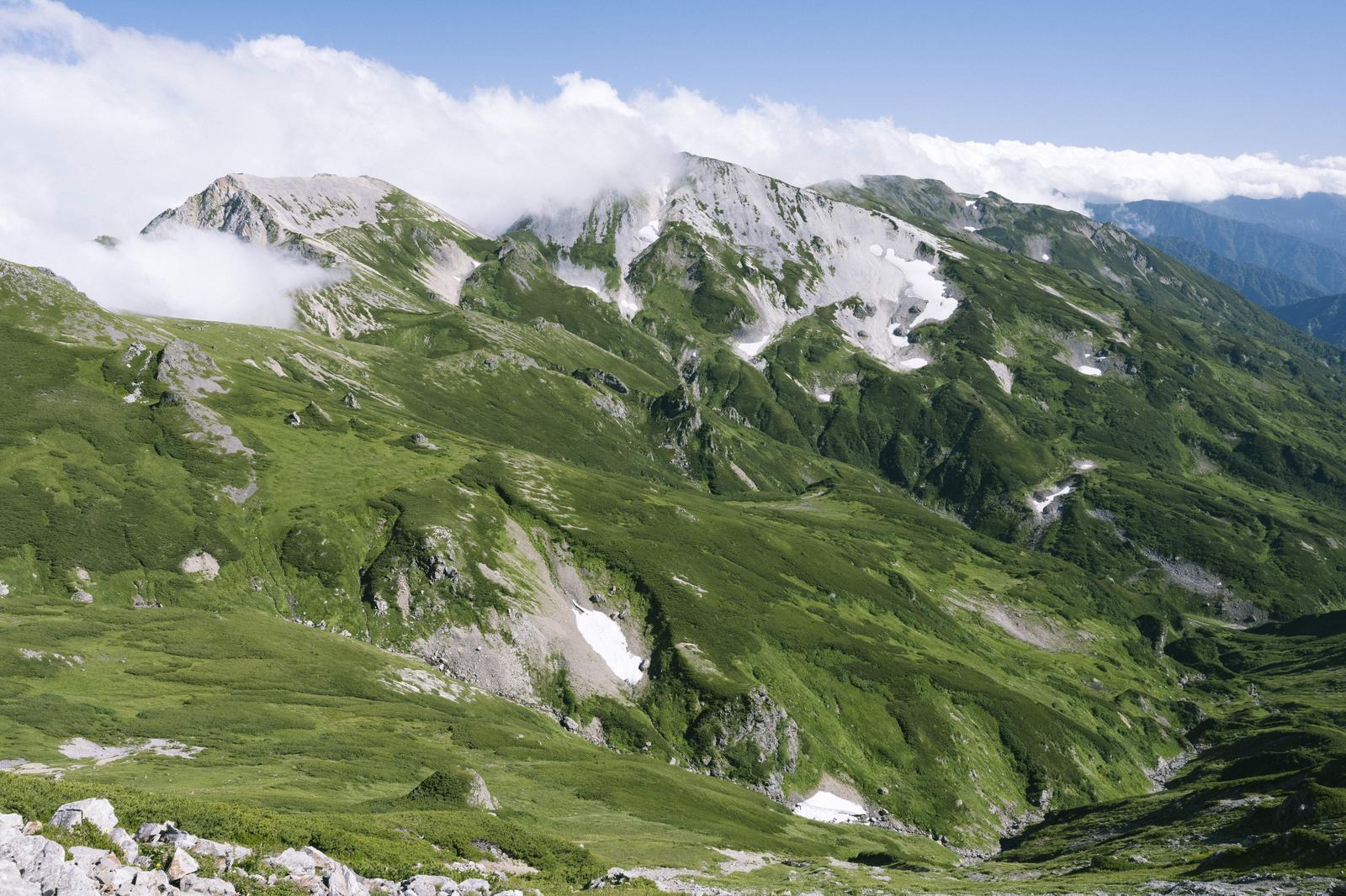 白馬三山の山肌に残る白い雪と緑の草地が広がる風景