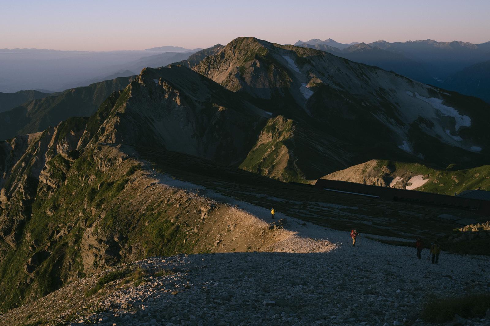 北アルプスの白馬岳付近で登山道を歩くハイカーたちと夕焼けに染まった山脈